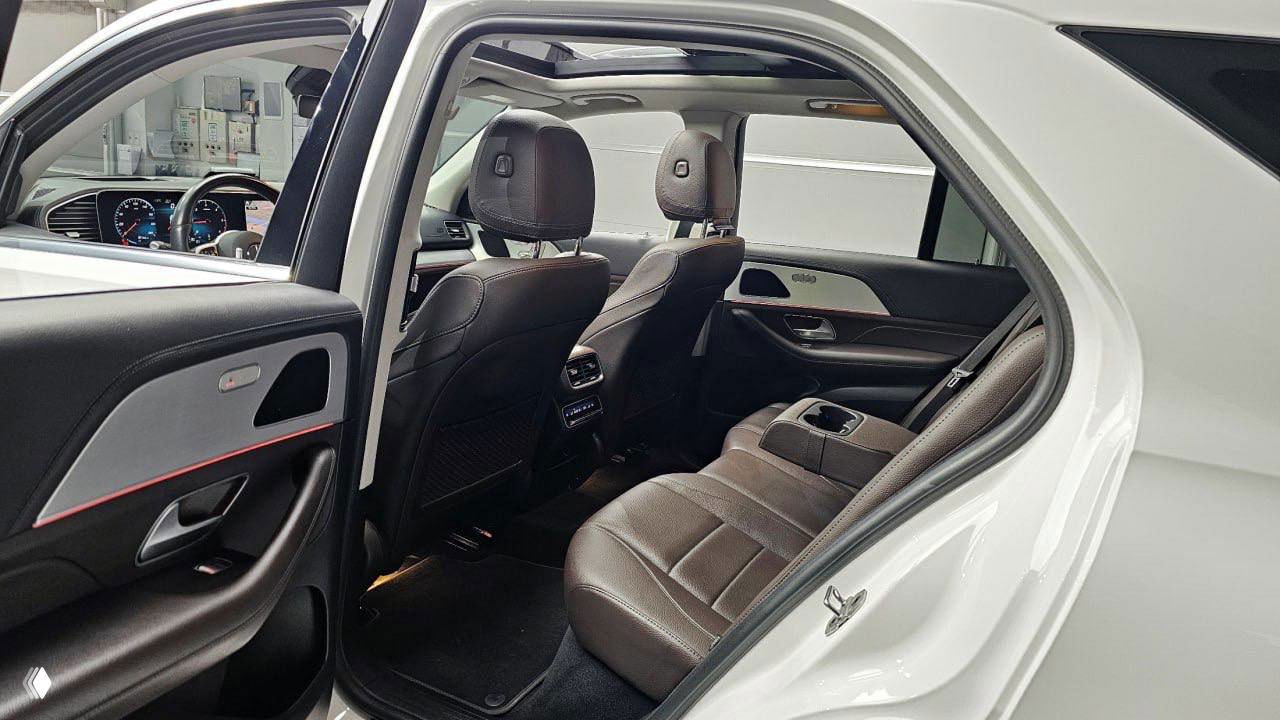 Задний салон Mercedes‑Benz GLE: задние сиденья, центральный подлокотник и панорамная крыша, видна отделка дверей и пространство для ног.