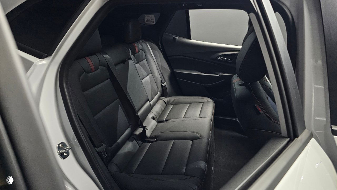 Задний ряд сидений белого Chevrolet Trax — чёрная обивка, вид через открытую заднюю дверь, состояние салона и места для пассажиров.