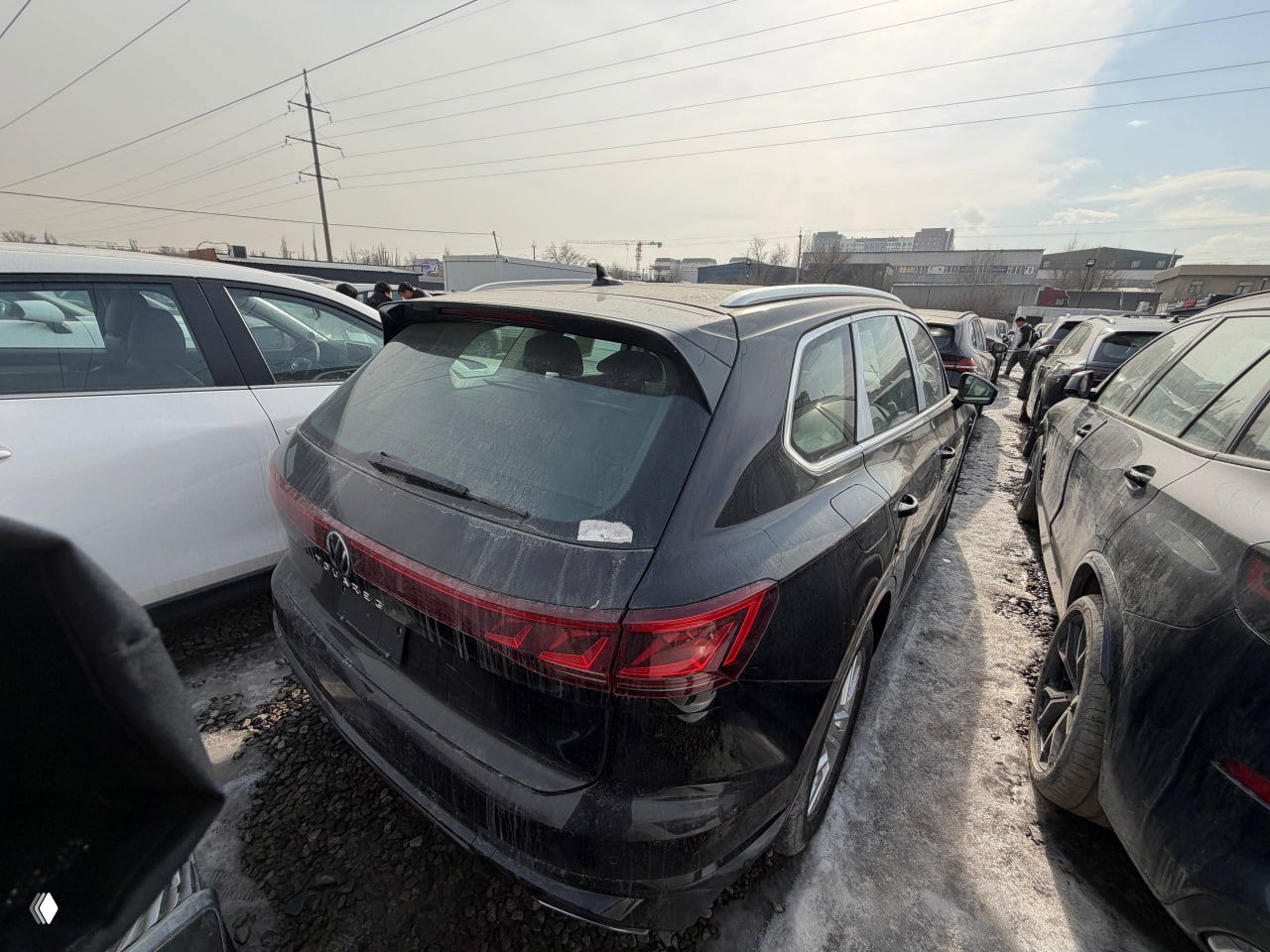 Фото задней части Touareg с небольшого расстояния, видна грязь на кузове, пустая монтажная табличка номера и общая парковочная зона.