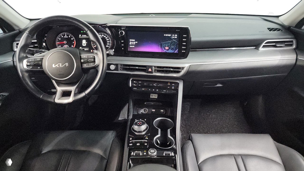 Интерьер Kia K5: приборная панель и широкий мультимедийный экран, чёрная отделка, руль с логотипом Kia и элементы управления