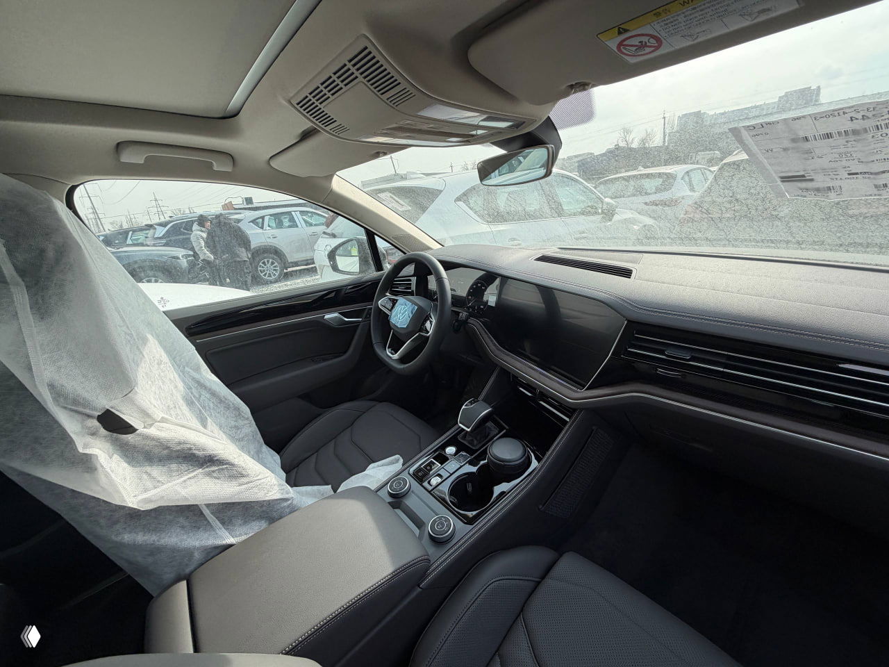 Общий ракурс задней части и крыши чёрного Volkswagen Touareg, вокруг другие автомобили и индустриальный фон автосклада.