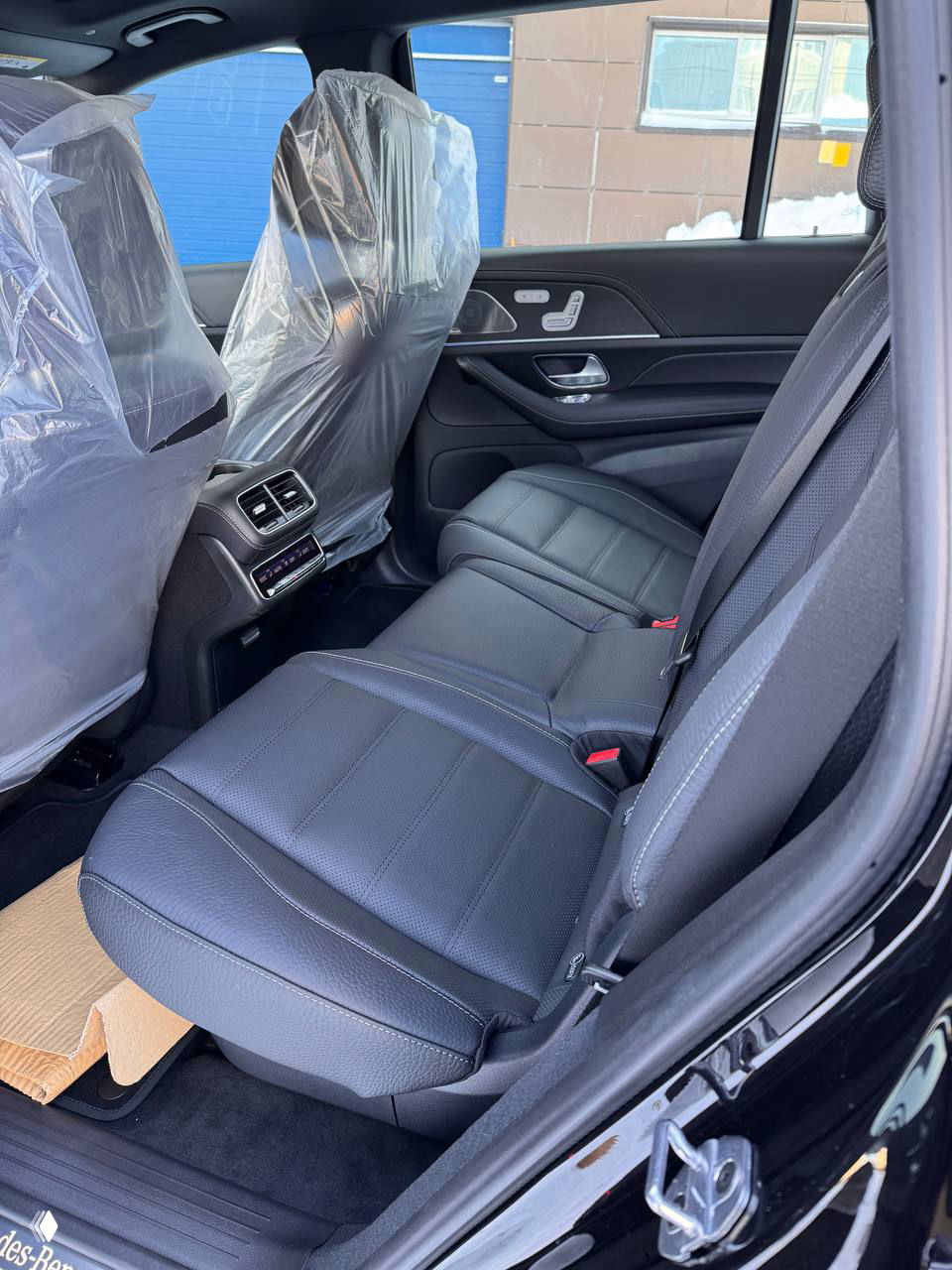 Вид на рулевую колонку и большой объединённый экран приборов и мультимедиа GLS 450d, защитные плёнки на сидении и обзор пространства перед автомобилем.