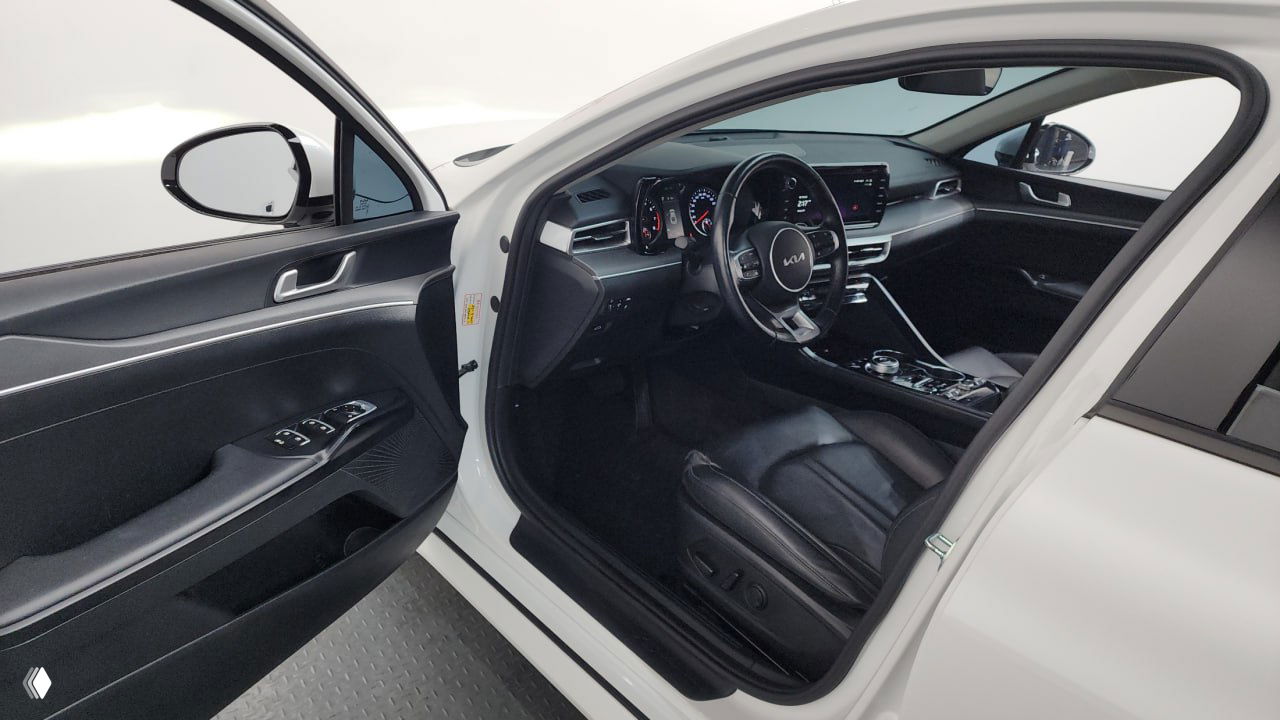Вид на переднюю пассажирскую часть через открытую дверь Kia K5: переднее сиденье, дверная карта, центральная консоль и элементы управления