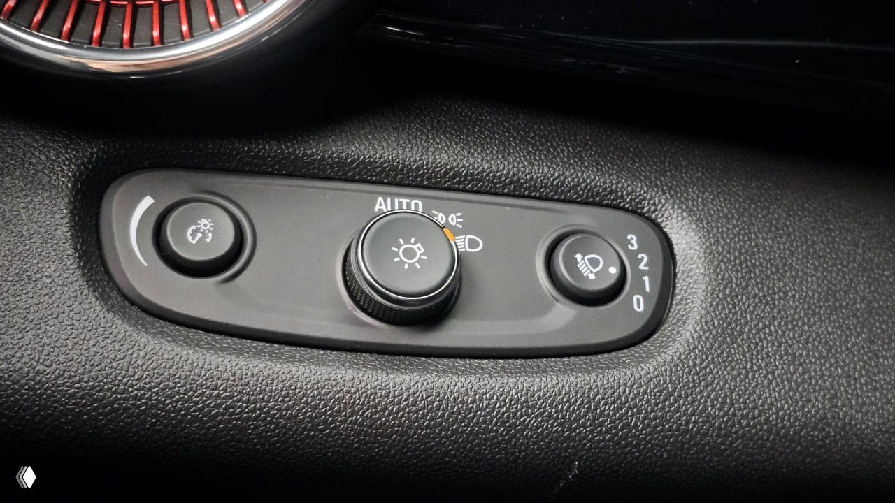 Крупный план регуляторов освещения и регулировки фар в салоне Chevrolet Trax, текстура панели и маркировка режимов видна чётко.