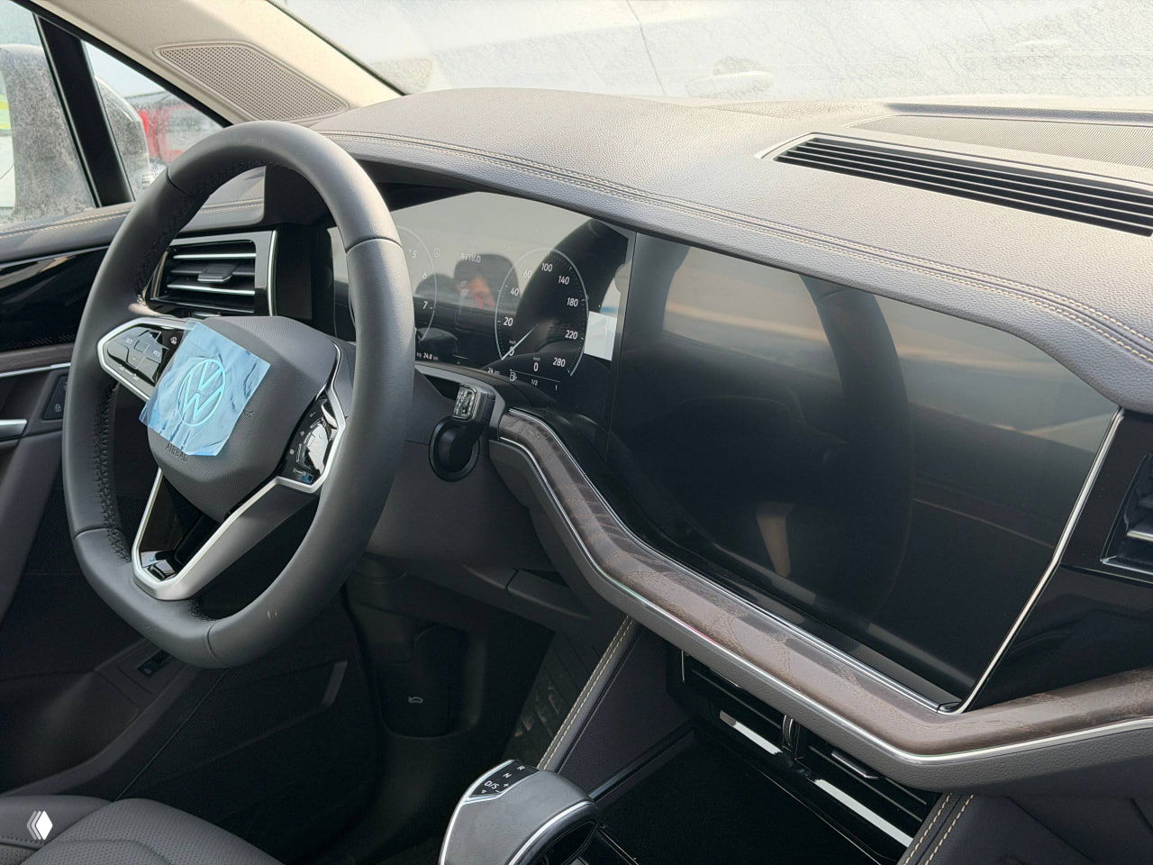 Панель водителя Volkswagen Touareg с рулём под плёнкой, крупный сенсорный дисплей и цифровая приборная панель — вид из кабины.