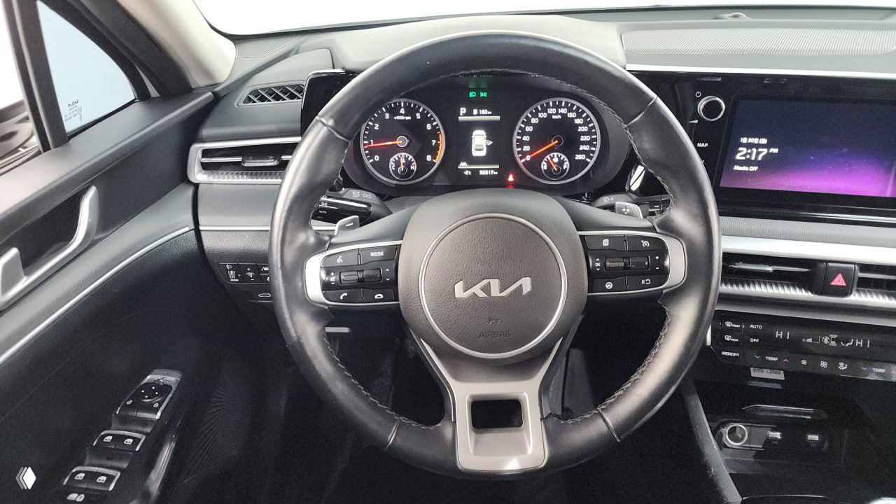 Крупный план руля Kia с логотипом, кнопками мультимедиа и частью приборной панели — область водителя и элементы управления в кадре