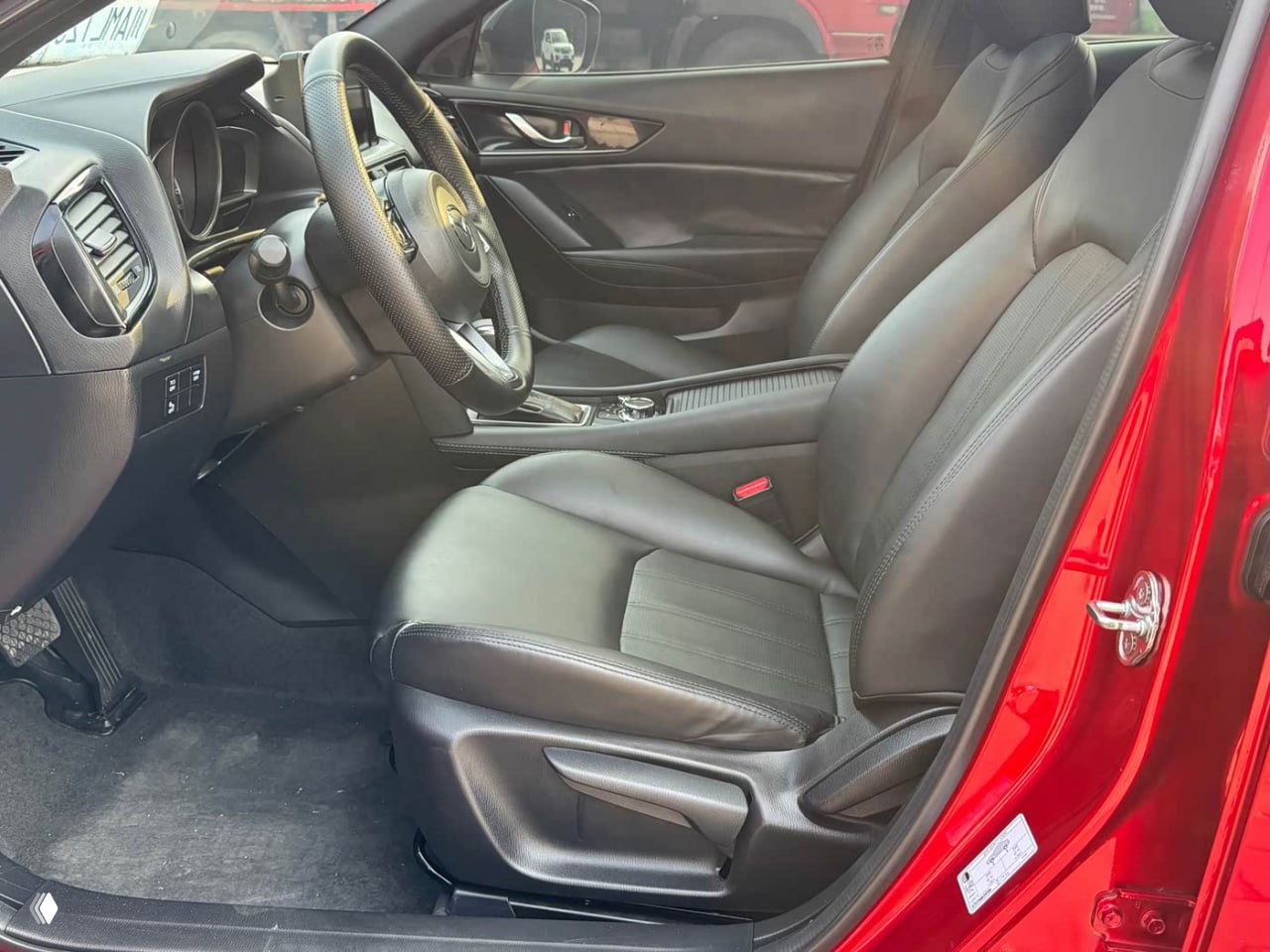 Водительское сиденье Mazda CX-4 в кожаной обивке, видны регулировки сиденья, руль и часть дверной карты с декоративной отделкой.