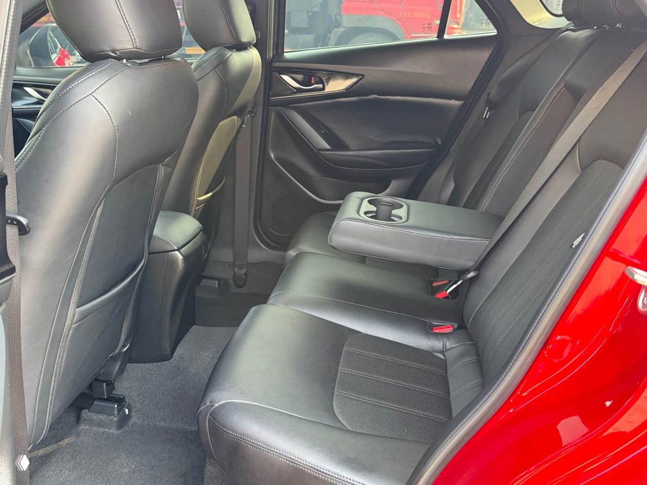 Задний ряд сидений Mazda CX-4 в чёрной обивке с откинутым подлокотником и подстаканниками, достаточно ровный ковёр и аккуратные панели дверей.