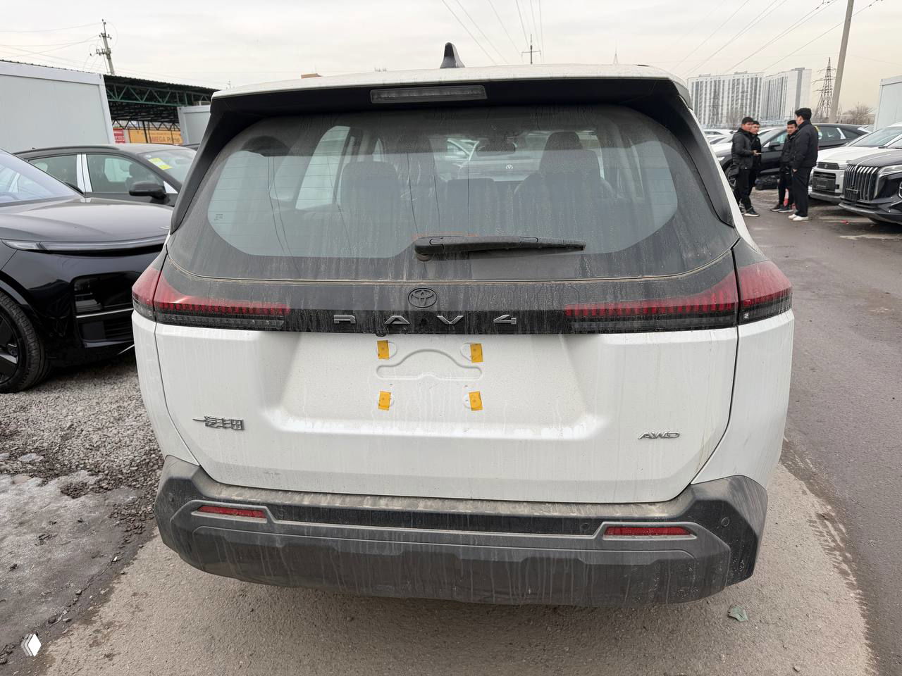 Задняя часть белого Toyota RAV4 с видимой надписью RAV4 и грязью на кузове, ракурс подчёркивает багажную дверь и задние фонари.
