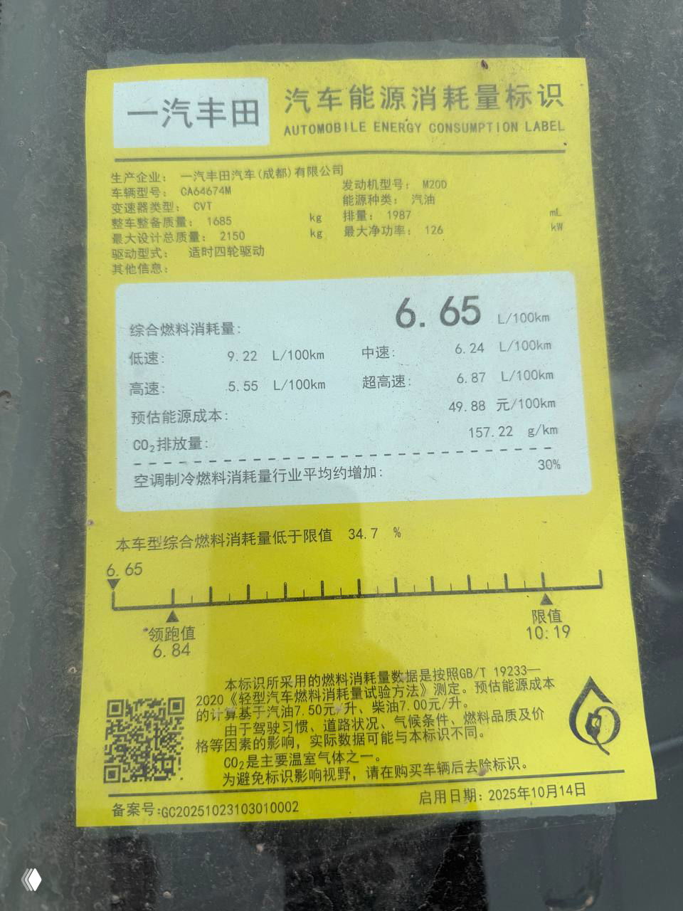 Жёлтая наклейка с маркировкой потребления топлива на стекле автомобиля — отметка 6.65 L/100km и другие данные о расходе и выбросах.