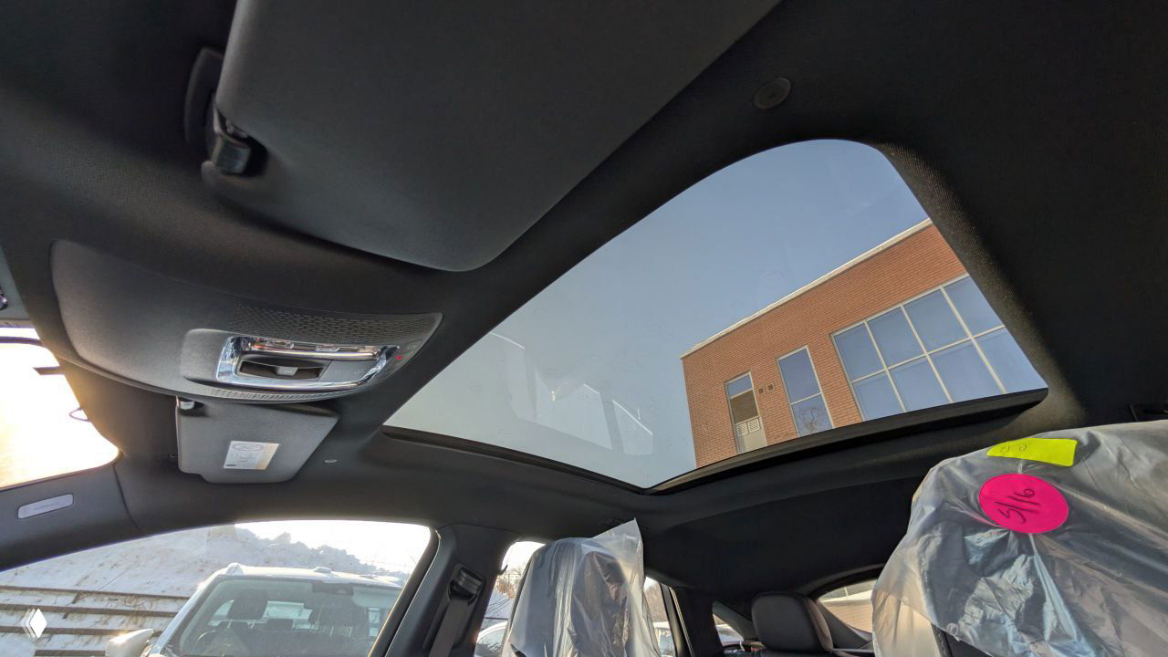 Вид из салона Mercedes‑GLE через панорамную крышу вверх; солнце и здание отражаются в стекле, видно защитные чехлы на сиденьях.