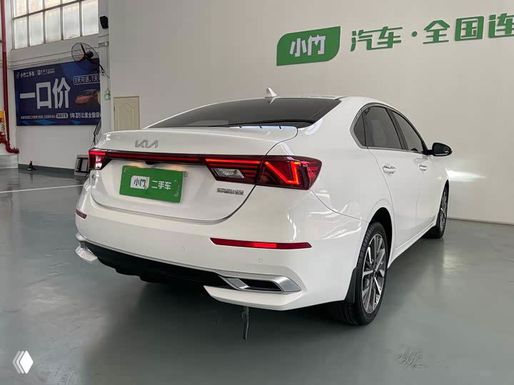 Задняя часть белого Kia K3 в автосалоне: видны фонари, бампер и выхлопная отделка, состояние лакокрасочного покрытия видно на фото.