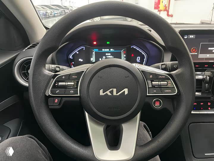 Крупный план руля Kia с логотипом KIA и клавишами управления, видна часть приборной панели за рулём и элементы управления.