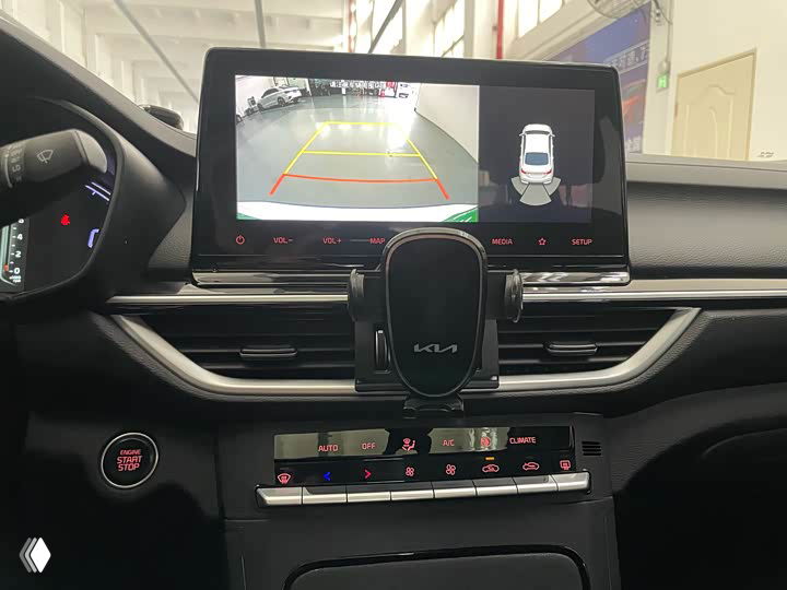 Центральная консоль Kia K3 с мультимедийным экраном, отображающим камеру заднего вида, и панелью управления климатом под экраном.