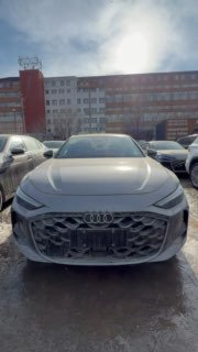 Фронтальный вертикальный кадр Audi A5L на парковке, машина стоит среди других автомобилей, видно переднюю часть и номерную рамку.