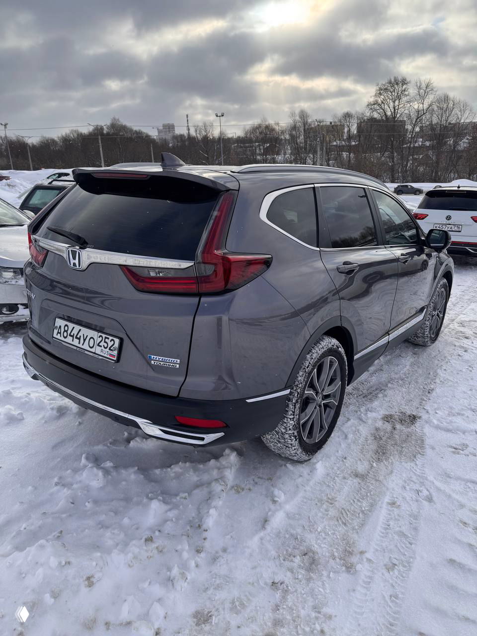 Задний трёхчетвертной вид Honda CR‑V 2021 в сером цвете, видна конструкция кузова, тонированные стёкла и колея на снегу вокруг автомобиля.