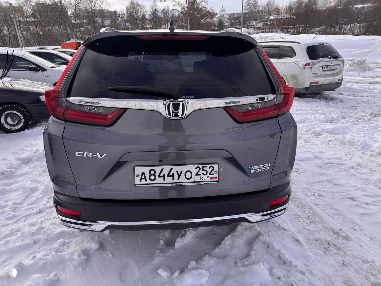 Вид сзади на багажник Honda CR‑V 2021: шильдик CR-V, эмблема Honda и регистрационная табличка на фоне снега на парковке.