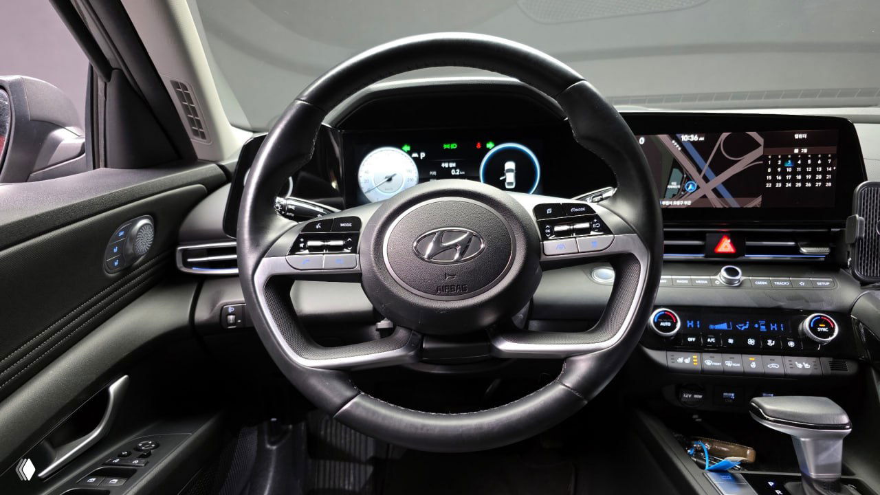 Крупный план руля и передней панели Hyundai AVANTE: вид на органы управления на руле, цифровую приборную панель и экран навигации справа.