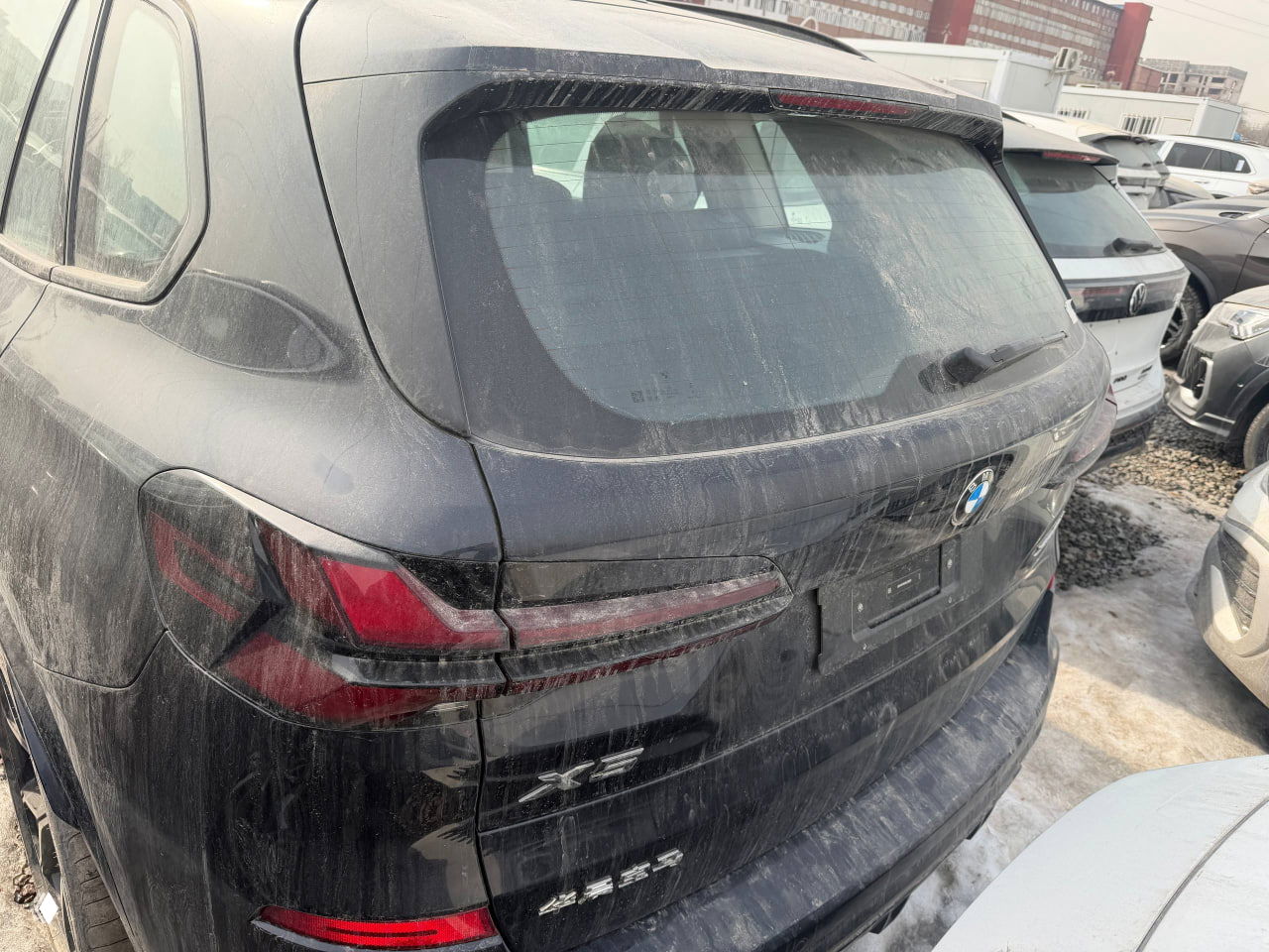 Вид сзади: грязная задняя часть чёрного BMW X5, видны задние фонари, эмблема X5 и белые номерные держатели без номеров.