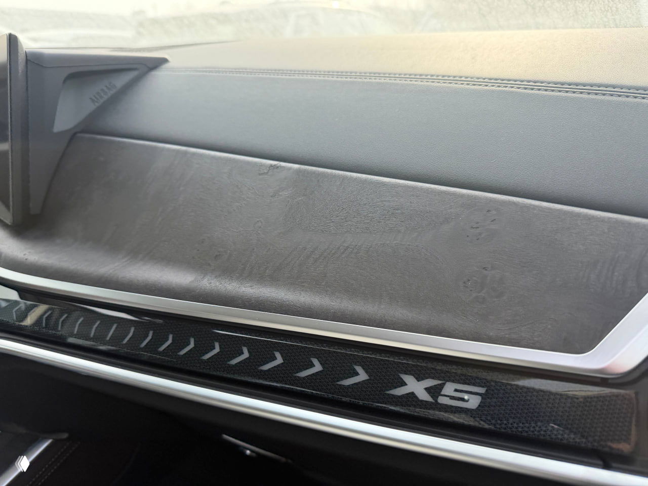 Деталь панели приборов с надписью X5 и верхней частью передней панели, видны следы транспортировочной упаковки и текстура отделки.