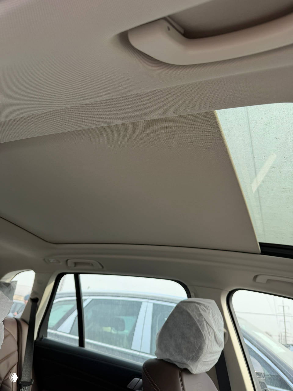 Потолок и панорамный люк в задней части салона BMW X5, видны ручки и защитные чехлы на задних подголовниках, фото сделано из салона.