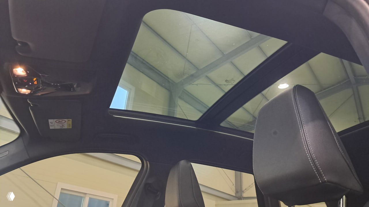 Панорамная крыша BMW X1: большое стационарное стеклянное пространство над передними сиденьями, видна внутренняя конструкция потолка и свет в ангаре.