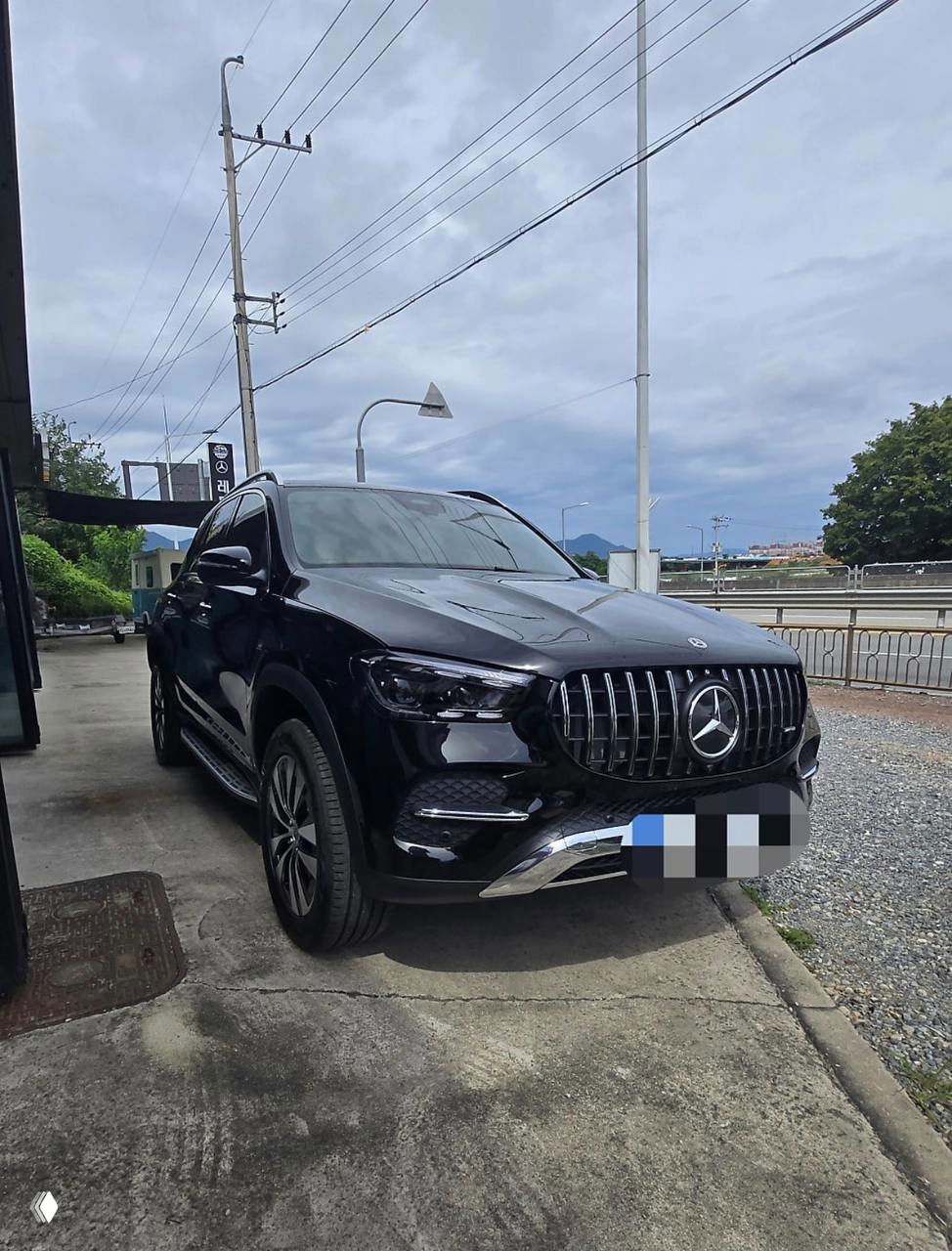 Трёхчетвертной вид чёрного Mercedes‑Benz GLE‑Class 350i 2025 года, автомобиль припаркован рядом с фирменным сервисом, общий план кузова.