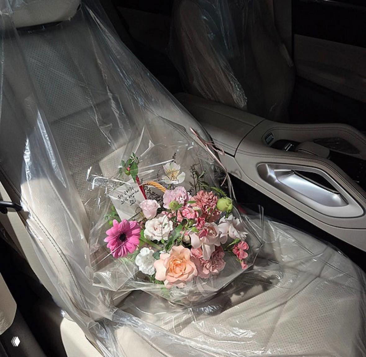 Букет цветов в полиэтиленовой упаковке, лежащий на пассажирском сиденье нового автомобиля — интерьер частично в защитной плёнке.