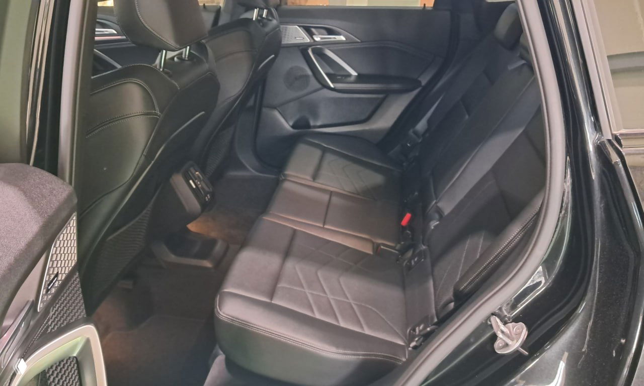 Задние сиденья BMW X1 в чёрной обивке: ровная посадка на троих, видна отделка дверных панелей и пространство для ног с подсветкой.