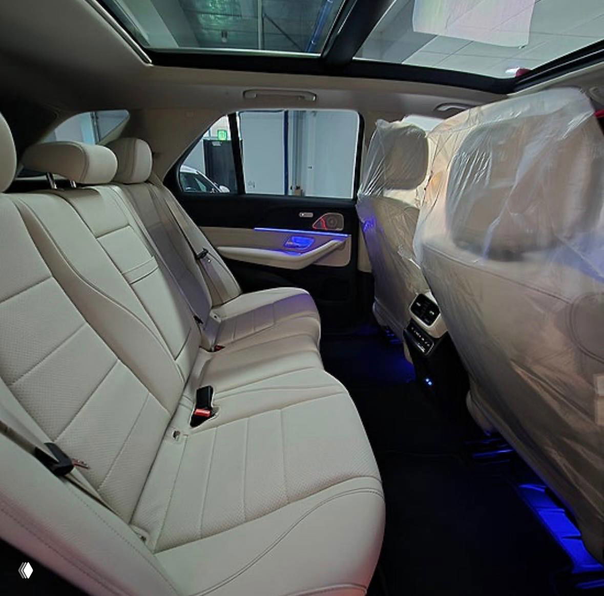 Задний ряд сидений Mercedes‑Benz GLE‑Class 350i с белой кожей и подсветкой, салон защищён упаковочной плёнкой, общий вид сидений и пространства.