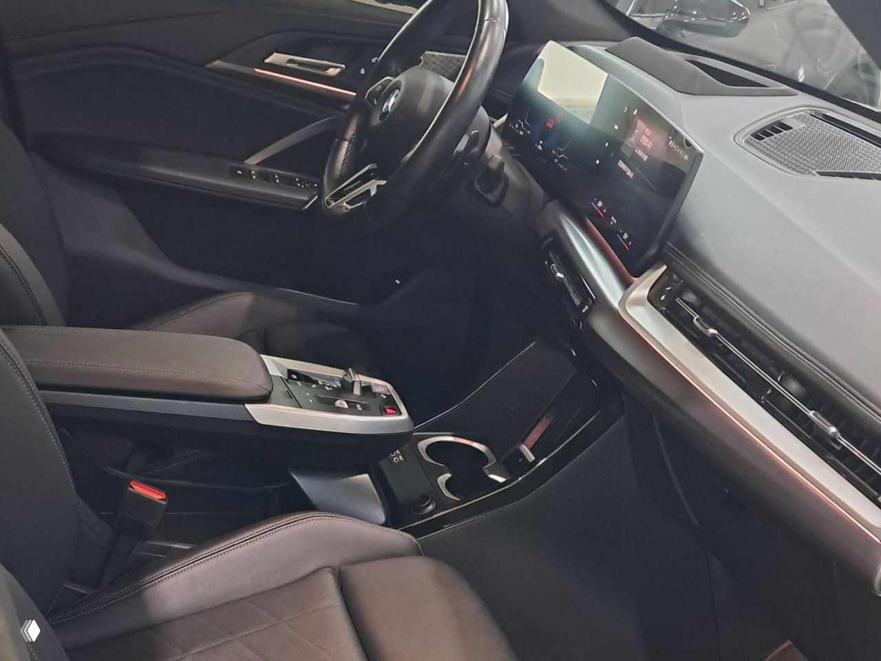 Вид на переднюю пассажирскую зону BMW X1: панель приборов, большой экран мультимедиа и чёрные декоративные вставки в интерьере автомобиля.