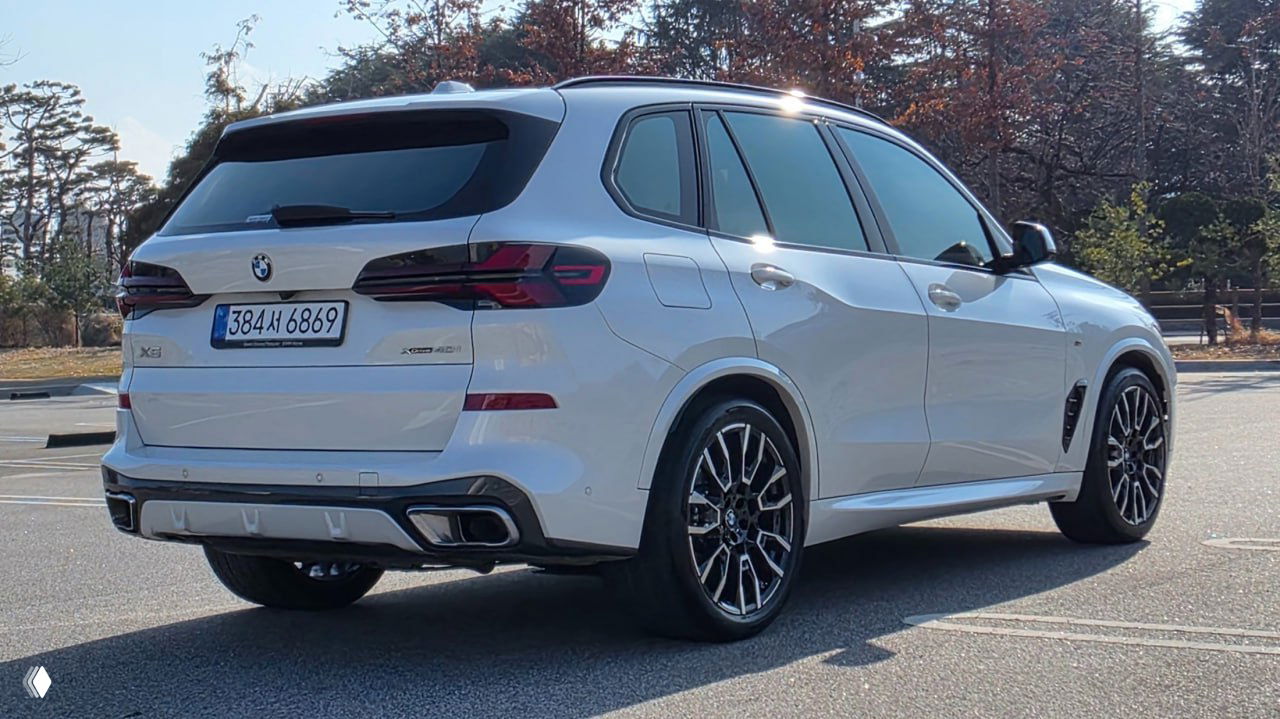 Белый BMW X5 xDrive 40i 2023 года, вид сзади и под углом, видна выхлопная система и задние фонари на дневной парковке.