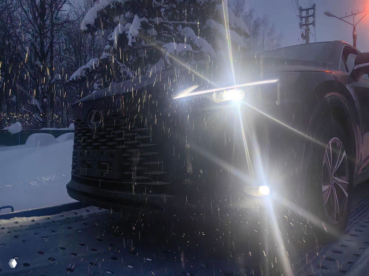 Фары Lexus RX 300 включены в снегопаде, снежные хлопья отражаются в свете, передняя часть автомобиля крупным планом и брызги снега.