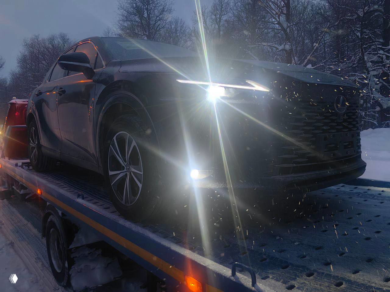 Лексус RX 300 вид спереди под углом, интенсивный свет фар и противотуманок, снег на капоте и дорожное покрытие с реагентом и следами эвакуатора.