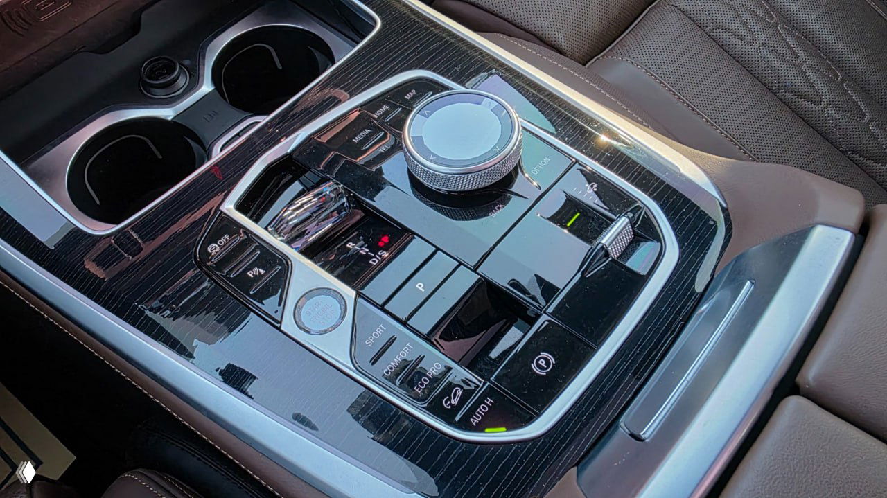 Крупный план центральной консоли BMW X5 xDrive 40i с джойстиком управления, переключателями режимов движения и отделкой под дерево.