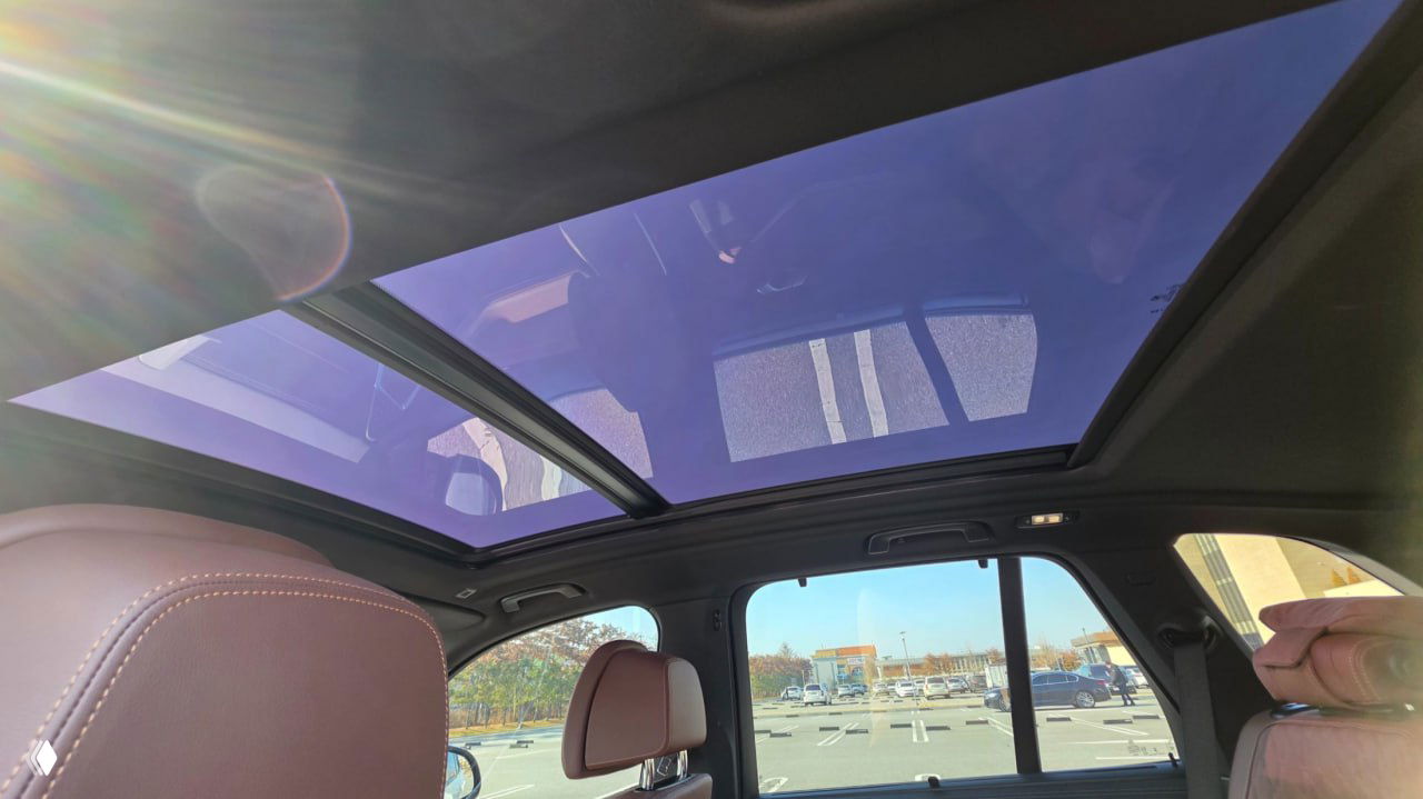 Панорамная крыша BMW X5 xDrive 40i — крупный вид на стеклянную поверхность крыши и свет в салоне, видно заднюю часть переднего ряда сидений.