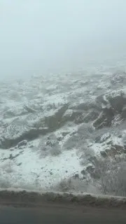 Плотный туман и следы снега на склоне перевала: низкая видимость, заснеженная обочина и размытые контуры горного рельефа.