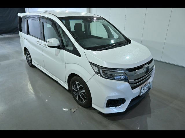 Фотография Honda Step Wagon в шоуруме под другим углом — видна передняя оптика, бампер, боковые зеркала и контуры капота.