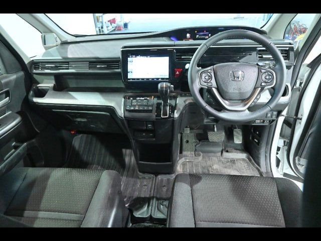 Интерьер Honda Step Wagon: крупный план панели приборов, руль, мультимедиа экран и центральная консоль с органами управления.