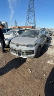 Вертикальная фотография Volkswagen Tharu XR под углом, человек рядом осматривает автомобиль на стоянке, индустриальный фон с опорами линий электропередачи.