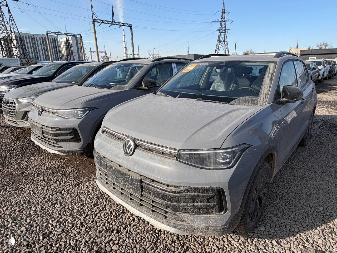 Фронтальный ракурс Volkswagen Tharu XR в ряду с другими SUV, солнечный день, машины припаркованы на гравии рядом с линиями электропередачи.