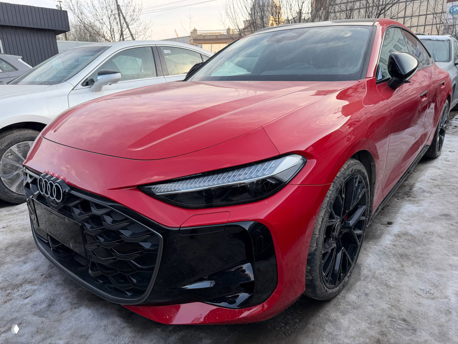 Красная Audi A5L вид спереди справа, парковка на улице со снегом, подчёркнута форма капота и передняя оптика автомобиля.