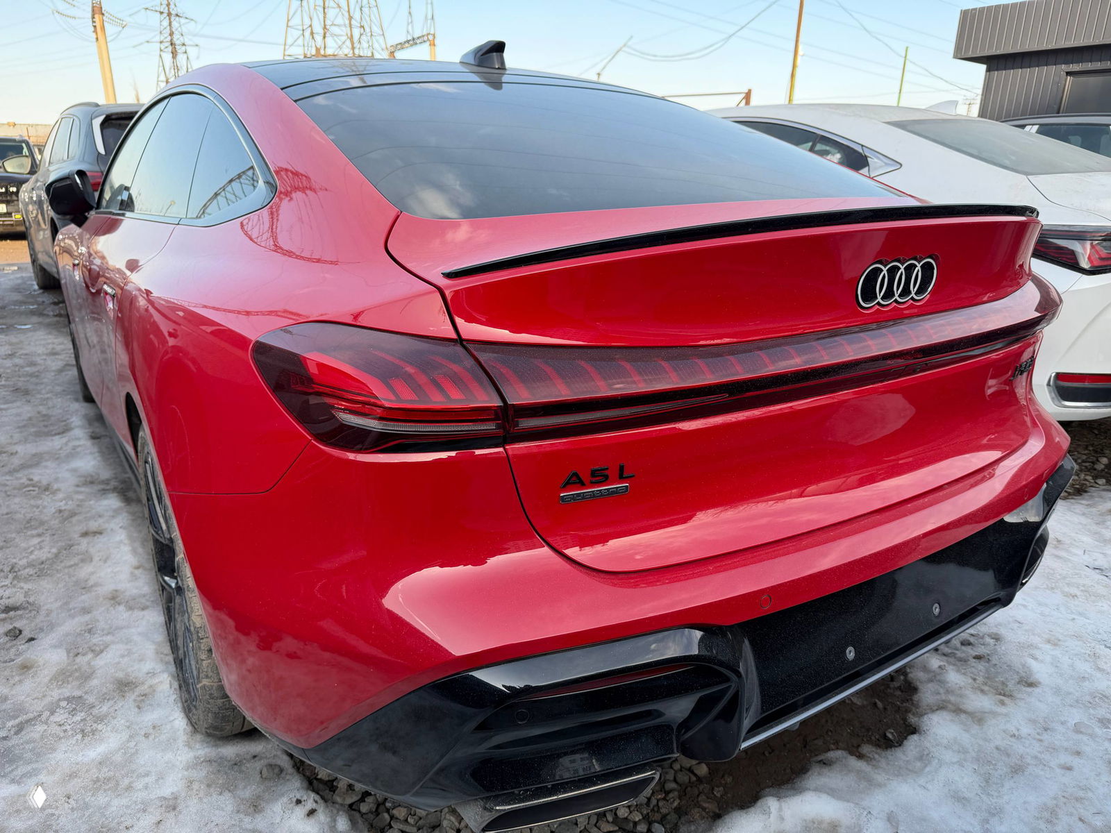 Задняя часть красной Audi A5L: спойлер, повторитель стоп-сигналов и шильдик A5L на багажнике, съемка на уличной стоянке.