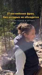 Портретная фотография улыбающейся женщины на тропе в лесу, видны камни и деревья; вертикальный кадр с естественным светом.