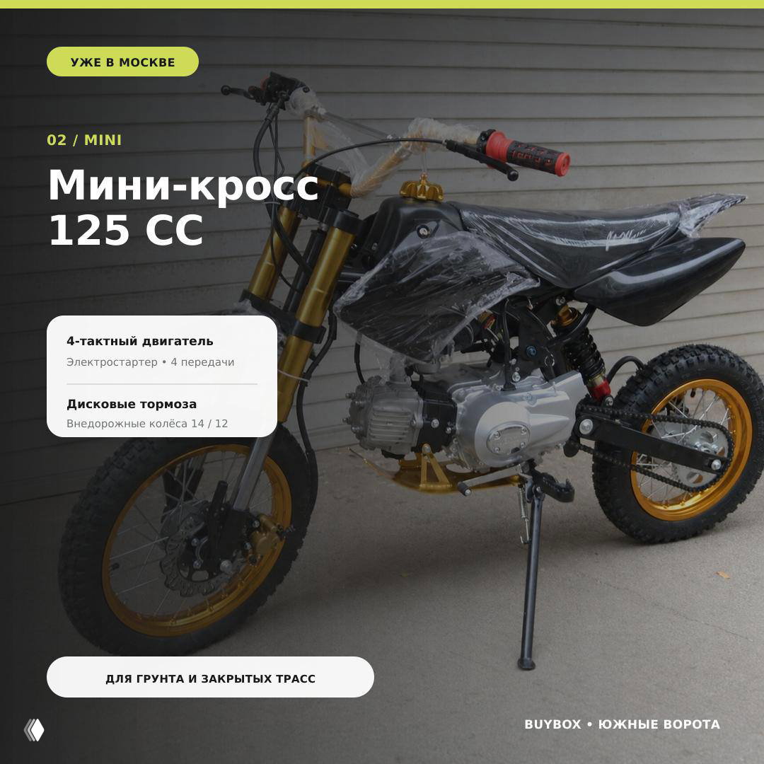 Мини-кросс 125 cc на серой площадке в заводской упаковке плёнкой и защитой, видно переднюю вилку, сиденье и частично двигатель.