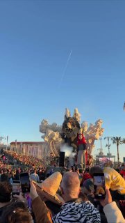 Парад на карнавале Вьяреджио: большая механическая фигура на платформе проезжает мимо трибун, публика снимает на телефоны и аплодирует.