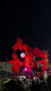 Красочная красная платформа с мифическим существом, театральной подсветкой и аплодирующей публикой на площади карнавала в Вьяреджио.