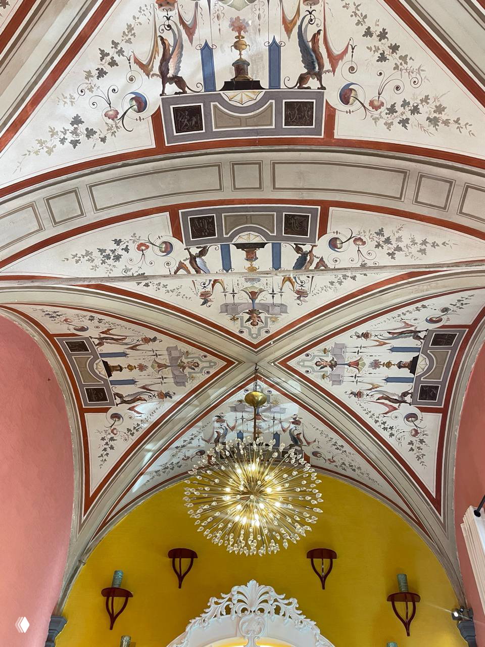 Декорованный свод потолка в бутике Aquazzura: фрески и орнаменты, центральная люстра и сочетание пастельных тонов стен и архитектуры.