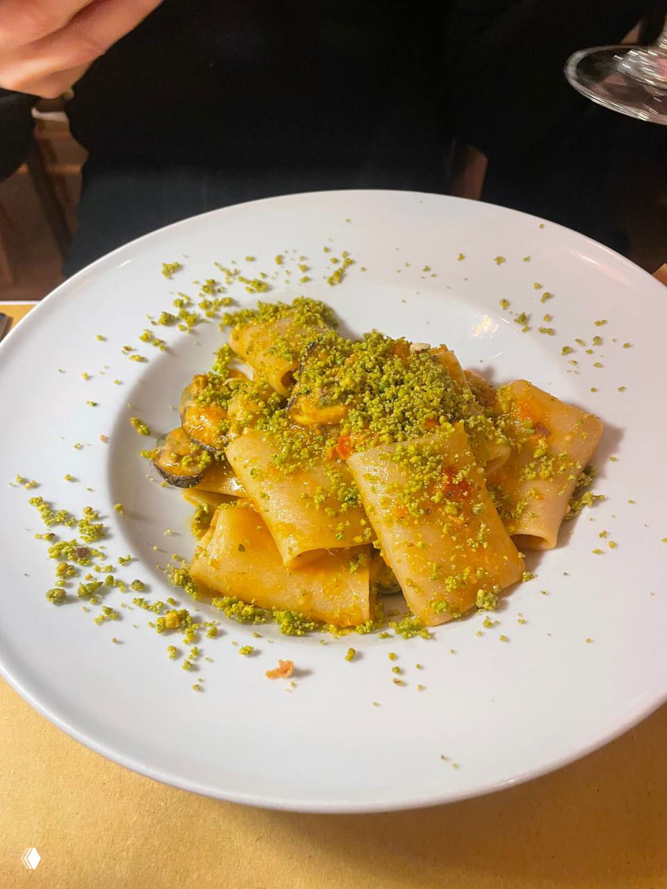 Тарелка пасты paccheri с крупной фисташковой крошкой сверху: крупные трубчатые макароны в соусе, украшенные измельчёнными фисташками.