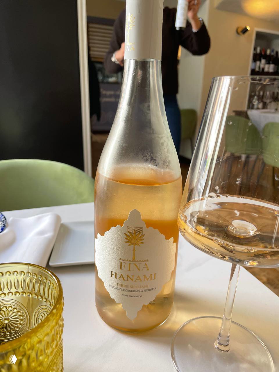 Крупный план: бутылка вина Fina Hanami и бокал на столе в ресторане; розоватый оттенок вина, читаемая этикетка Fina Hanami и часть сервировки рядом.